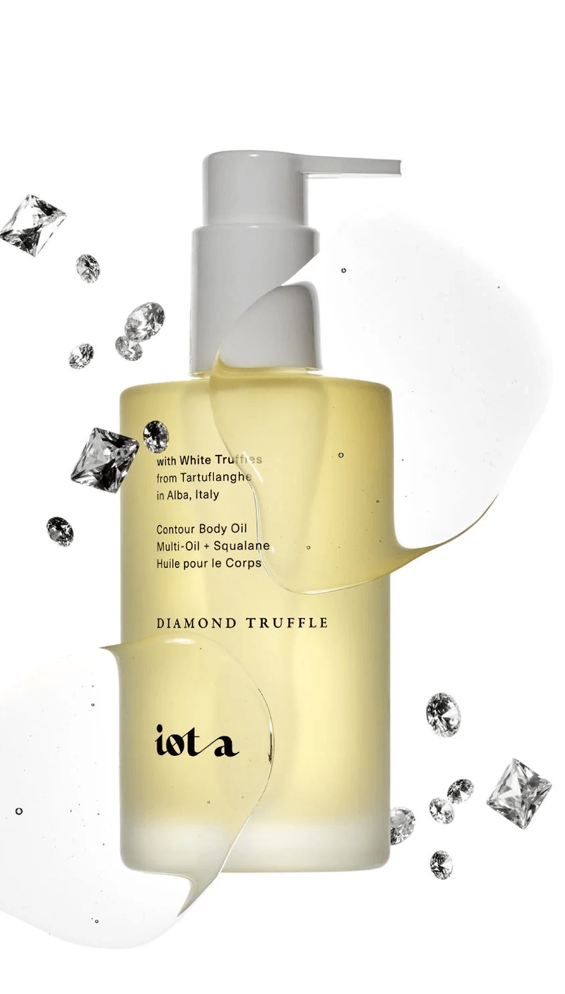 A bottle of IOMA Diamond Truffle contour body oil with a pump dispenser, surrounded by diamond-shaped and round crystals, and a splash of white oil in the background.