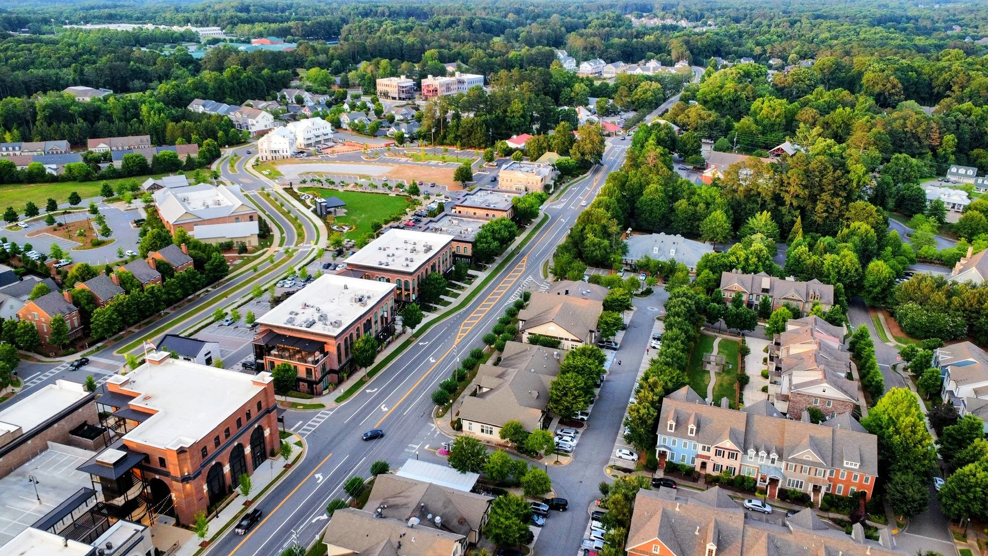Aerial view of a suburban area with a mix of residential houses, commercial buildings, green trees, and parking lots.