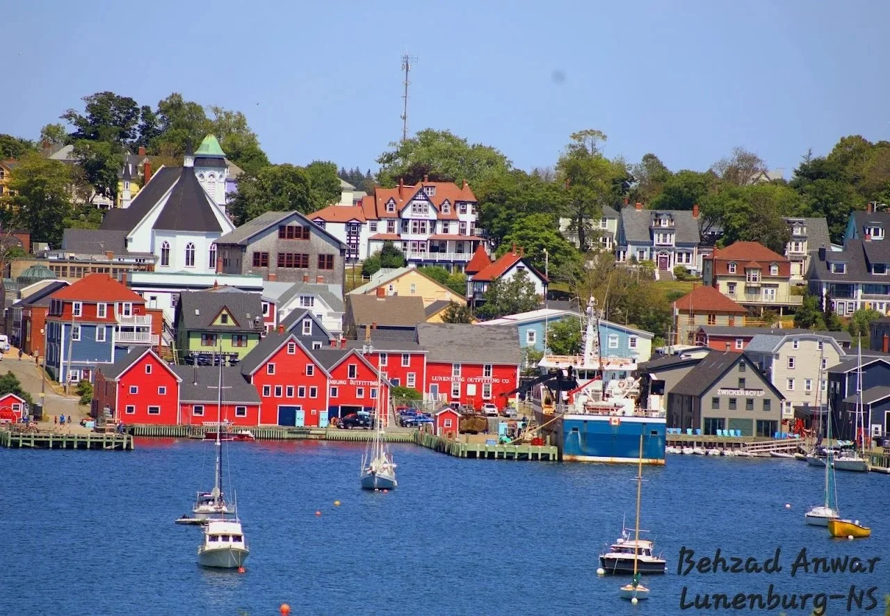 Colorful houses and boats in a seaside town, Lunenburg, Nova Scotia, with calm water and clear sky, mountains in the distance.
