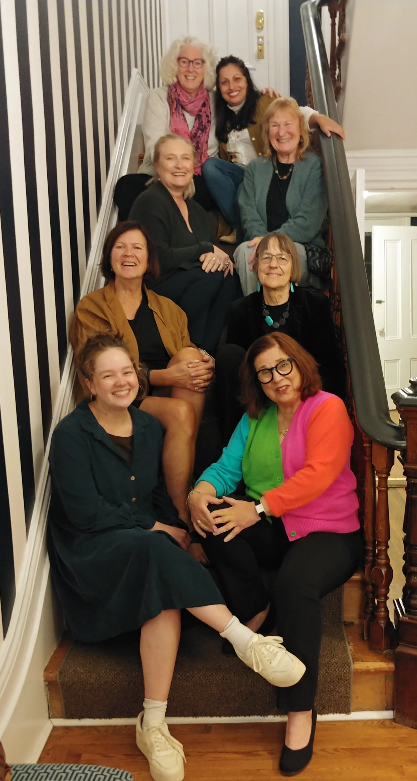 Group of ten women sitting on and standing around a staircase, smiling at the camera.