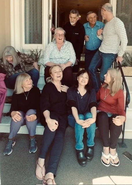 Group of seven women and men gathered on steps outside a house, laughing and talking.