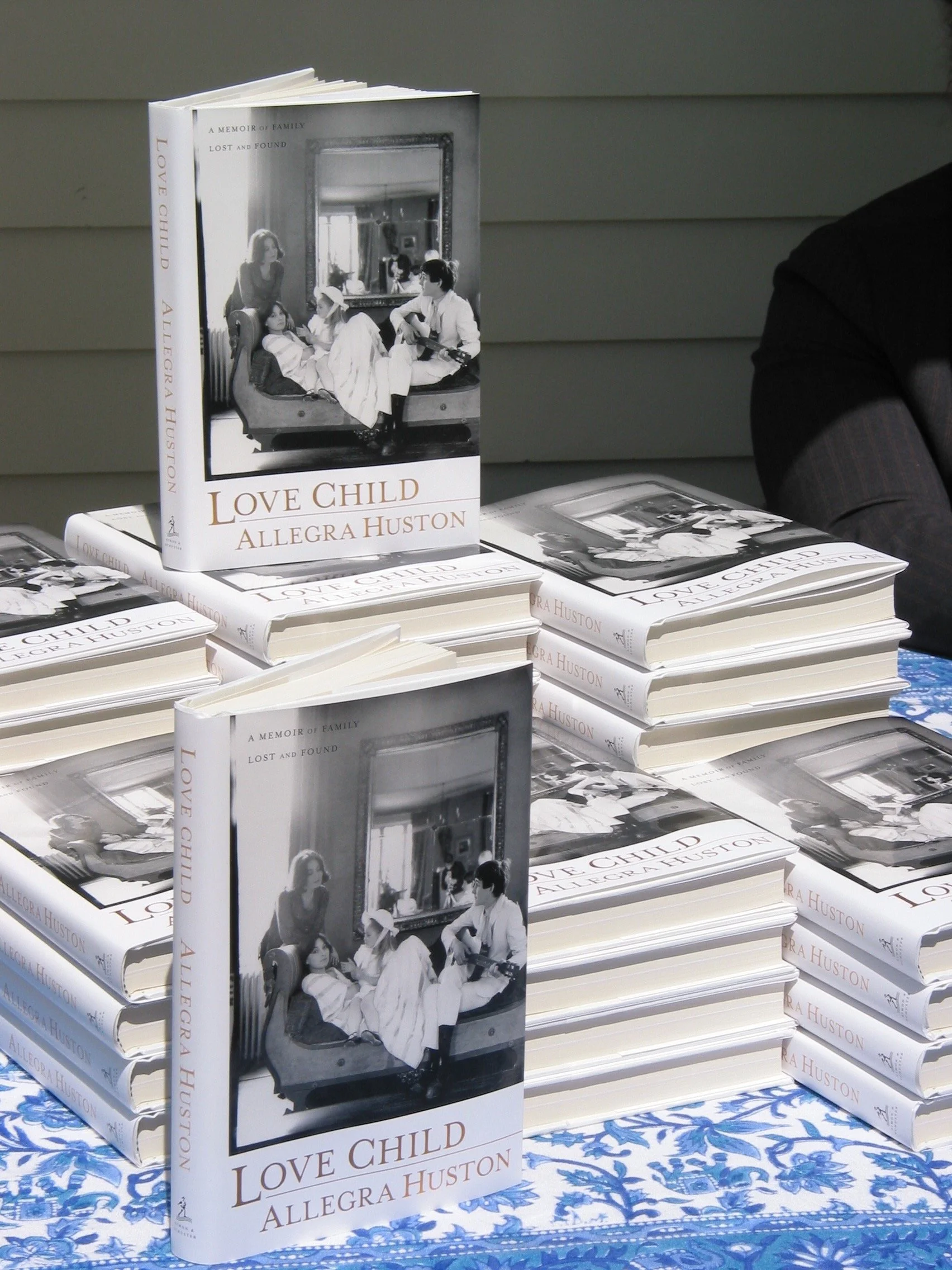 Books titled "Love Child" by Allegra Huston displayed on a table with a blue and white patterned tablecloth, stacked in multiple piles, with two copies standing upright.
