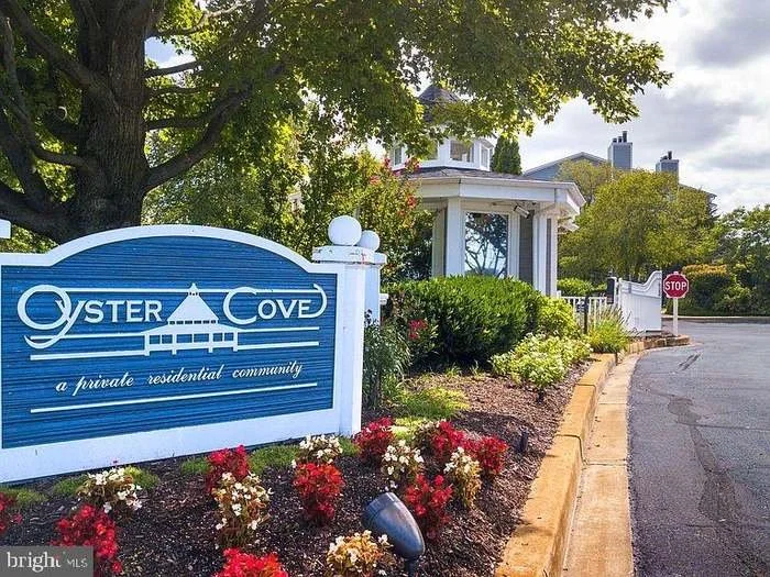Sign for Oyster Cove, a private residential community, with landscaped flowers and a house in the background.