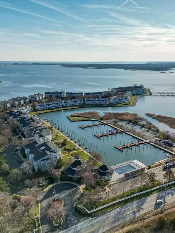 Aerial view of a lakeside marina with boats docks, surrounded by residential buildings and a waterway, under a partly cloudy sky.
