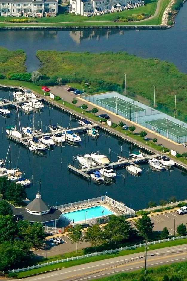 A marina with boats docked, a swimming pool, tennis courts, and surrounding greenery.