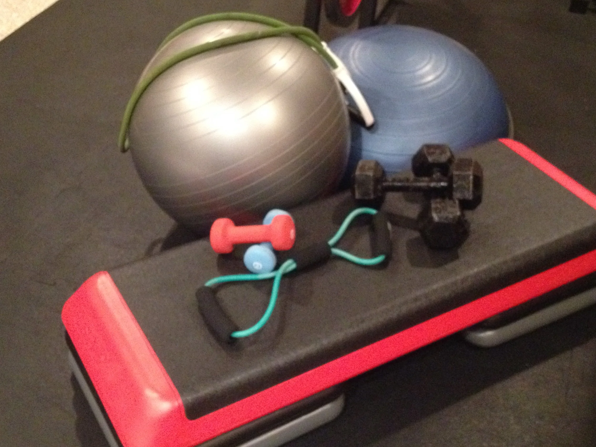 Living Wellness Boldly Personal training equipment  including two exercise balls, a small dumbbell, a jump rope, and two small dumbbells on a black and red exercise bench.
