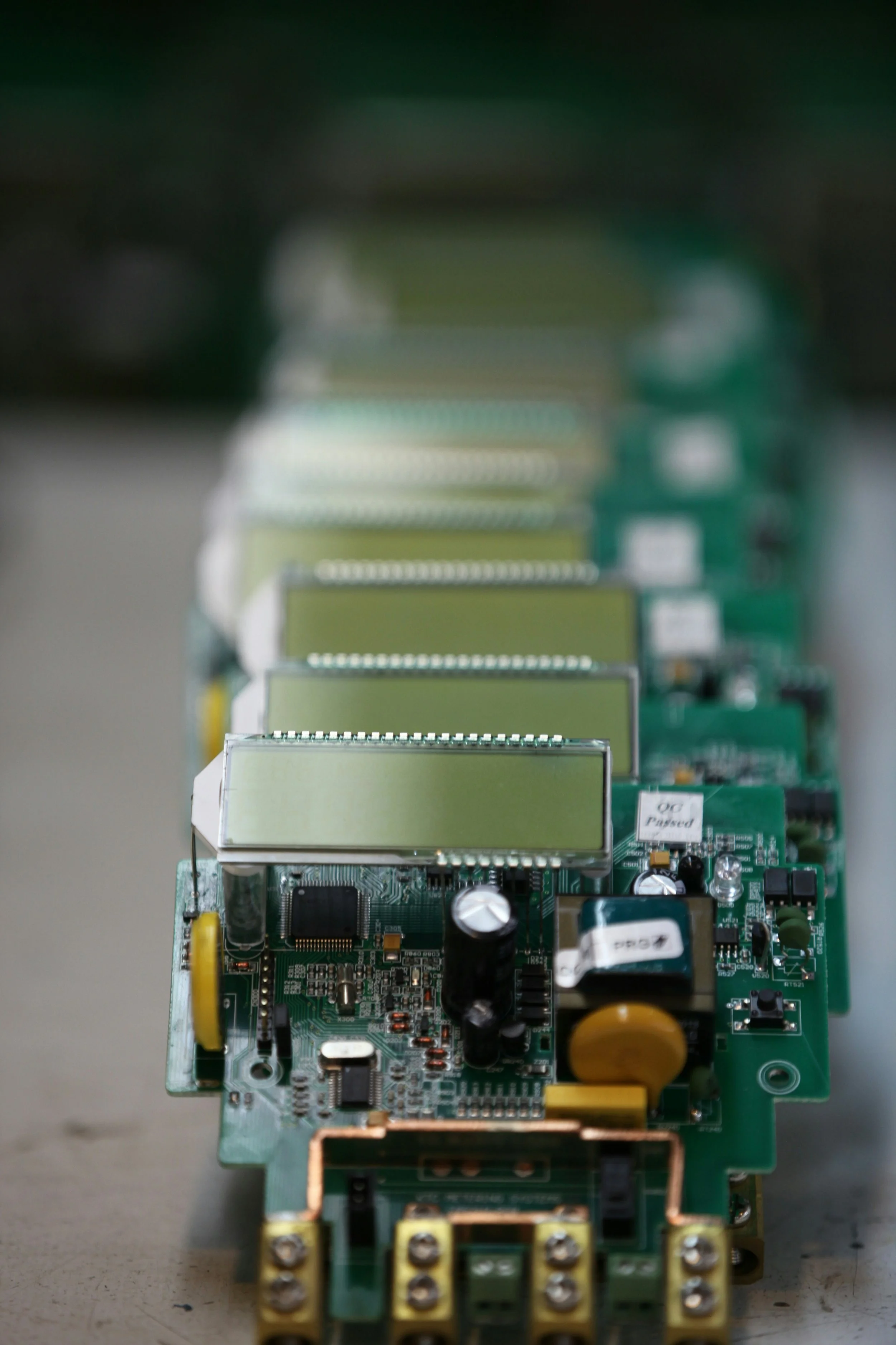 Close-up of multiple green printed circuit boards (PCBs) stacked in a row, featuring various electronic components such as capacitors, resistors, and chips.