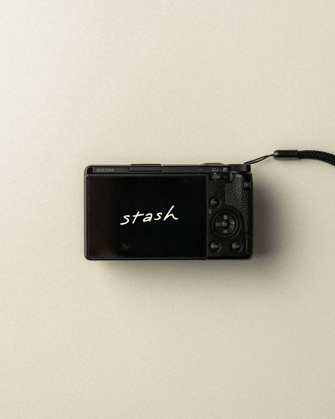 Digital camera on a plain, light-colored surface with the words "stash" written on the screen.