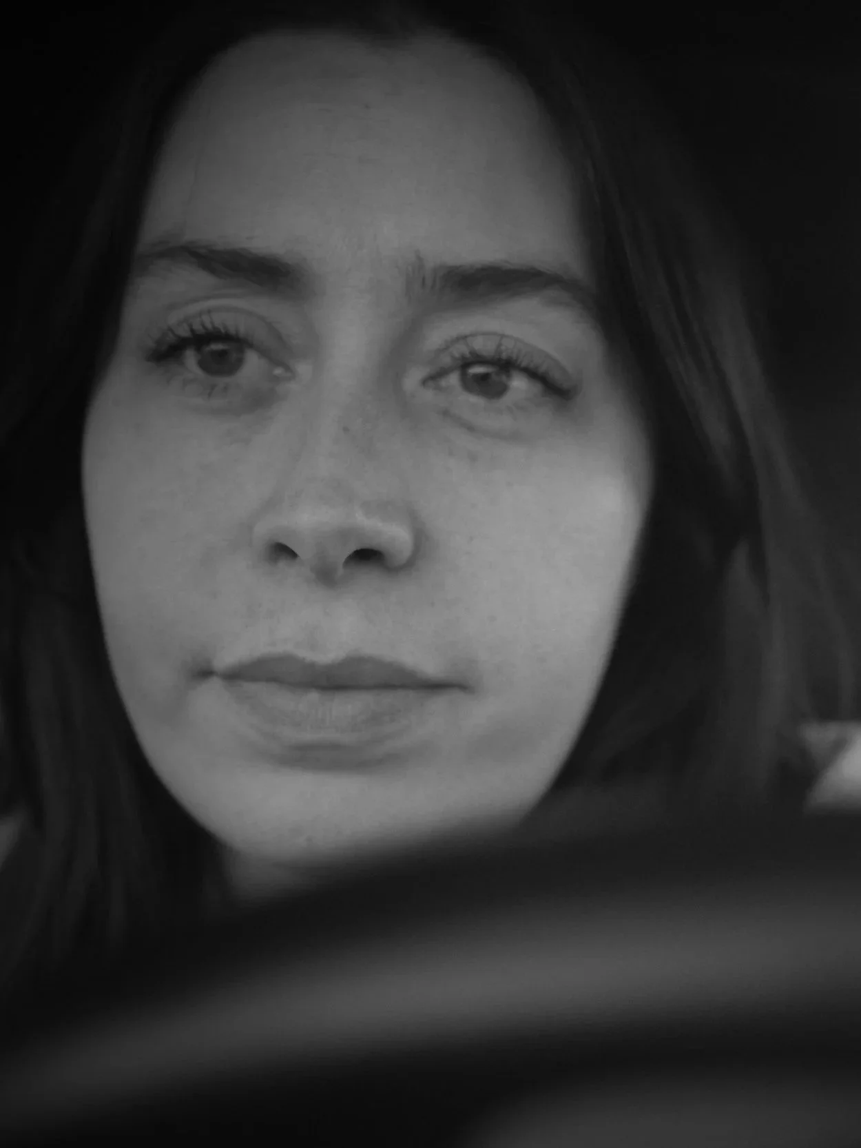 A close-up black and white photograph of a woman's face, with her eyes slightly looking to the side and her lips closed.