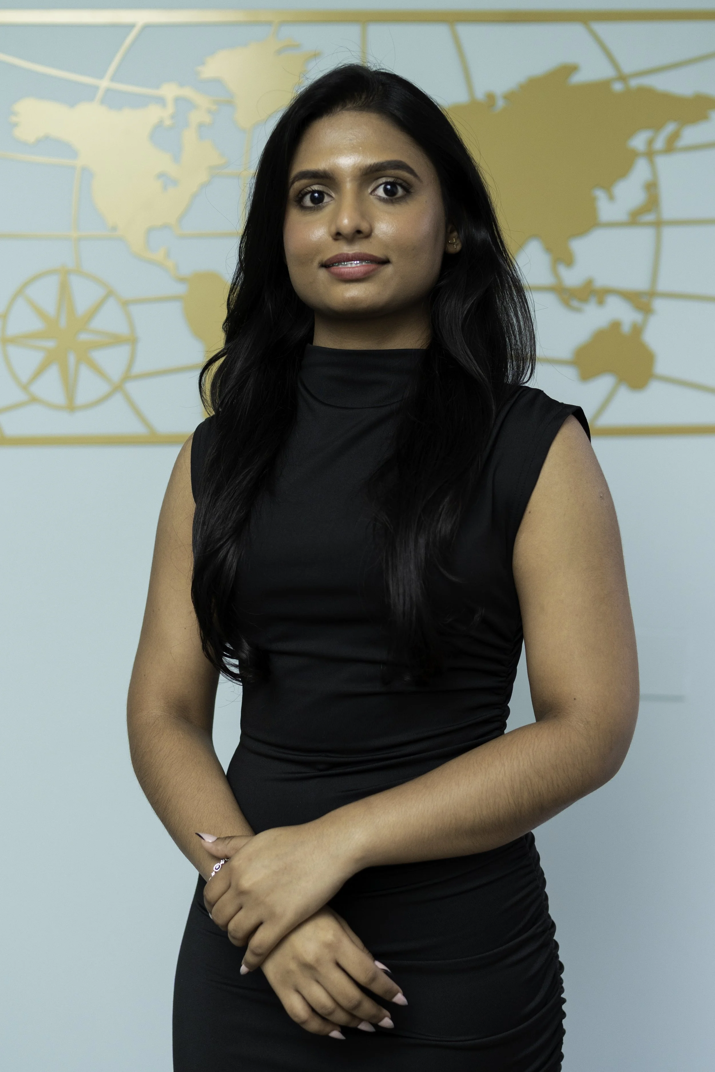 A woman with long black hair and a black sleeveless dress standing in front of a world map background.