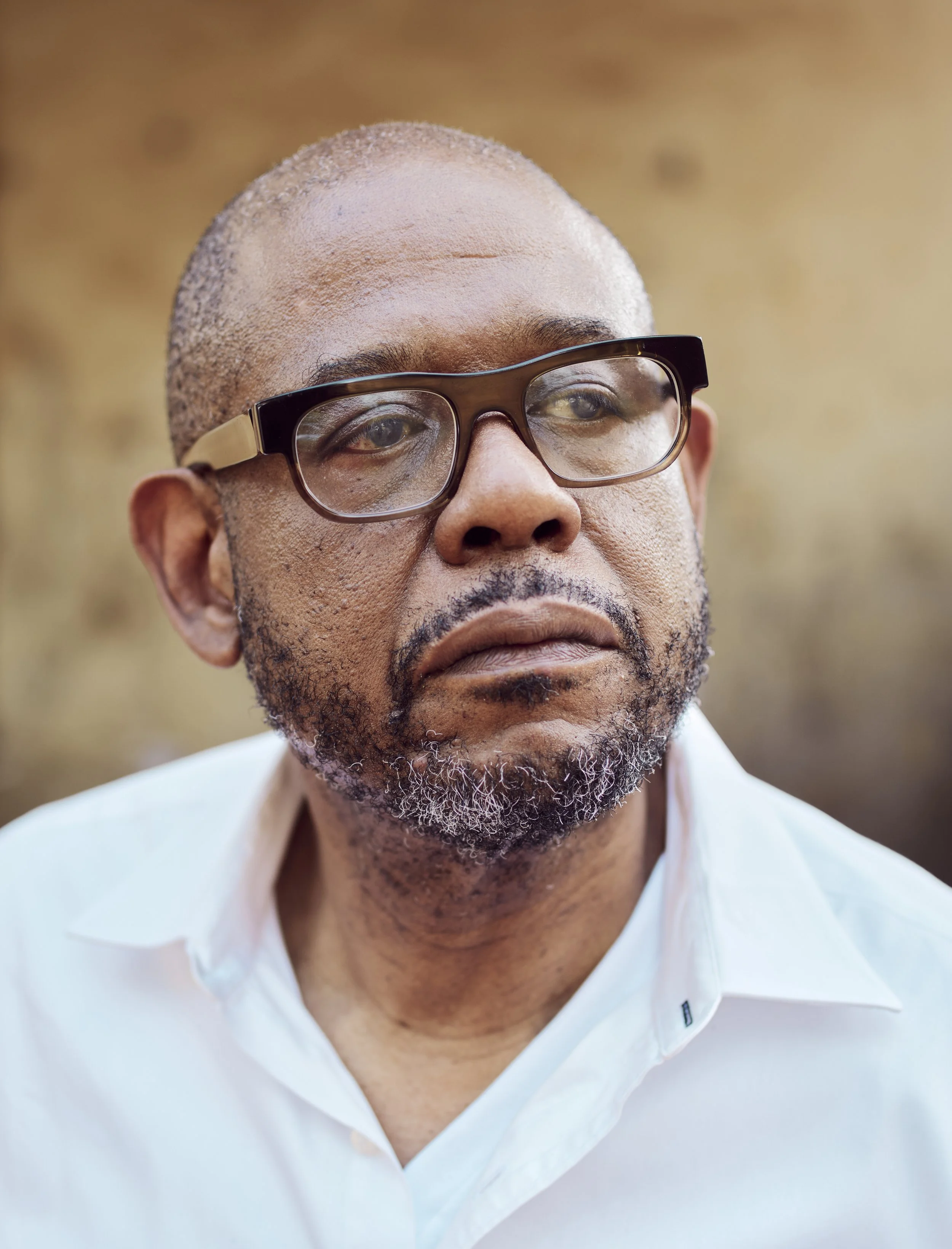 A middle-aged man with glasses and a beard, wearing a white shirt, with a serious expression, outdoors with a blurred background.