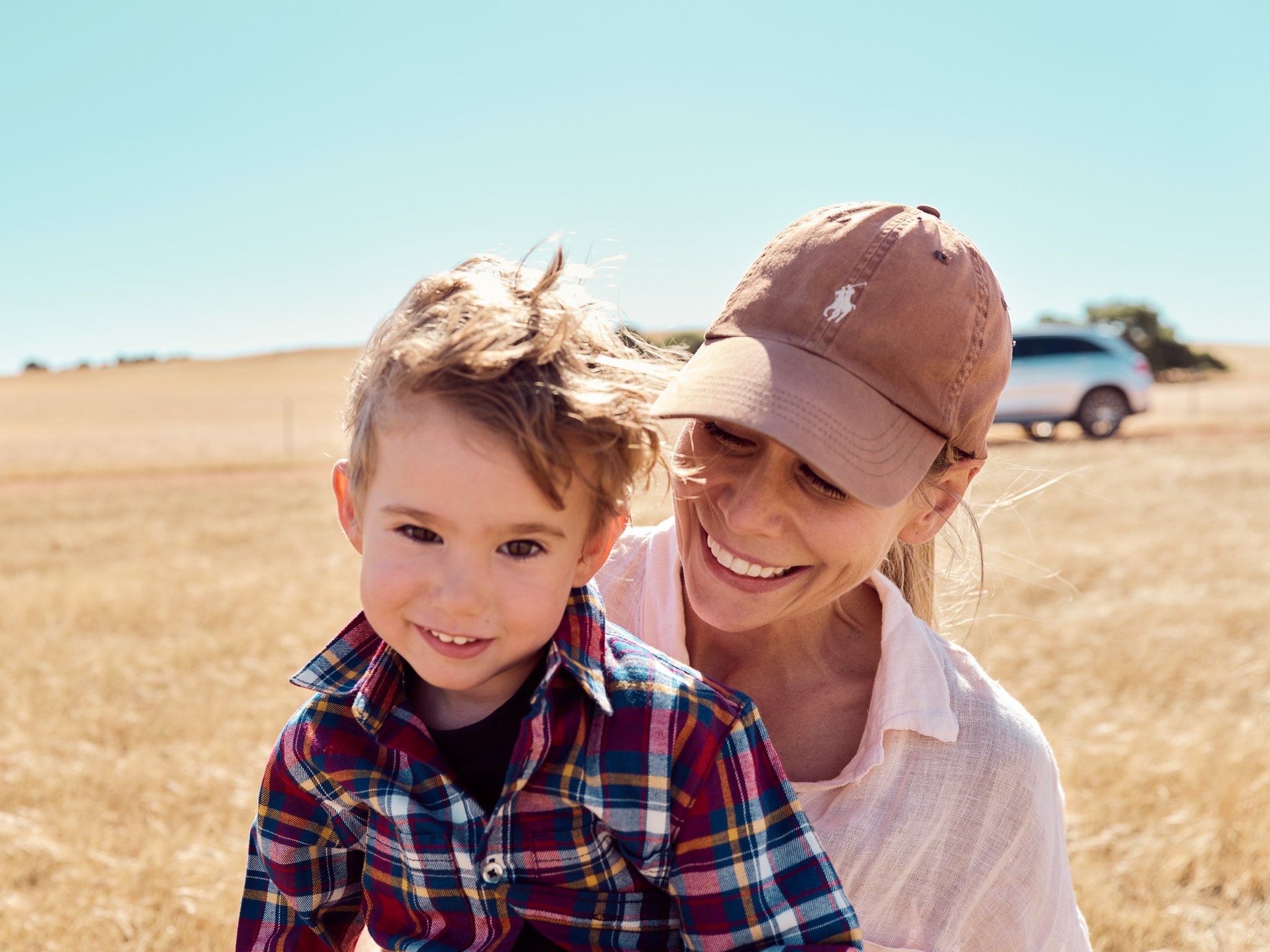 A smiling young boy and woman outdoors in a grassy field during the daytime.
