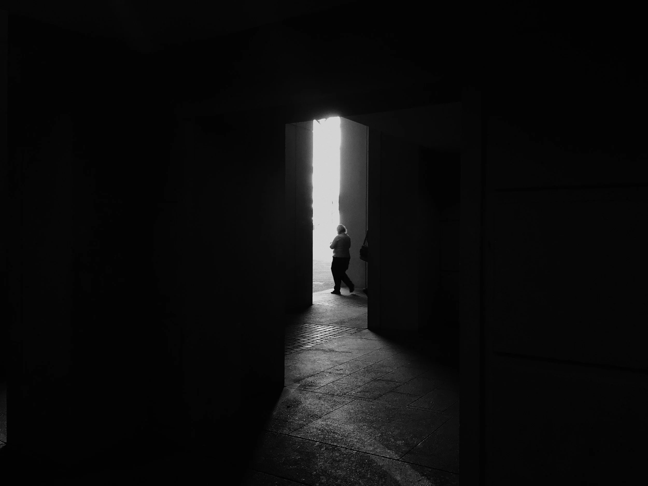 Una figura de un hombre de espaldas en una entrada con luz brillante que entra desde afuera, en un espacio oscuro.