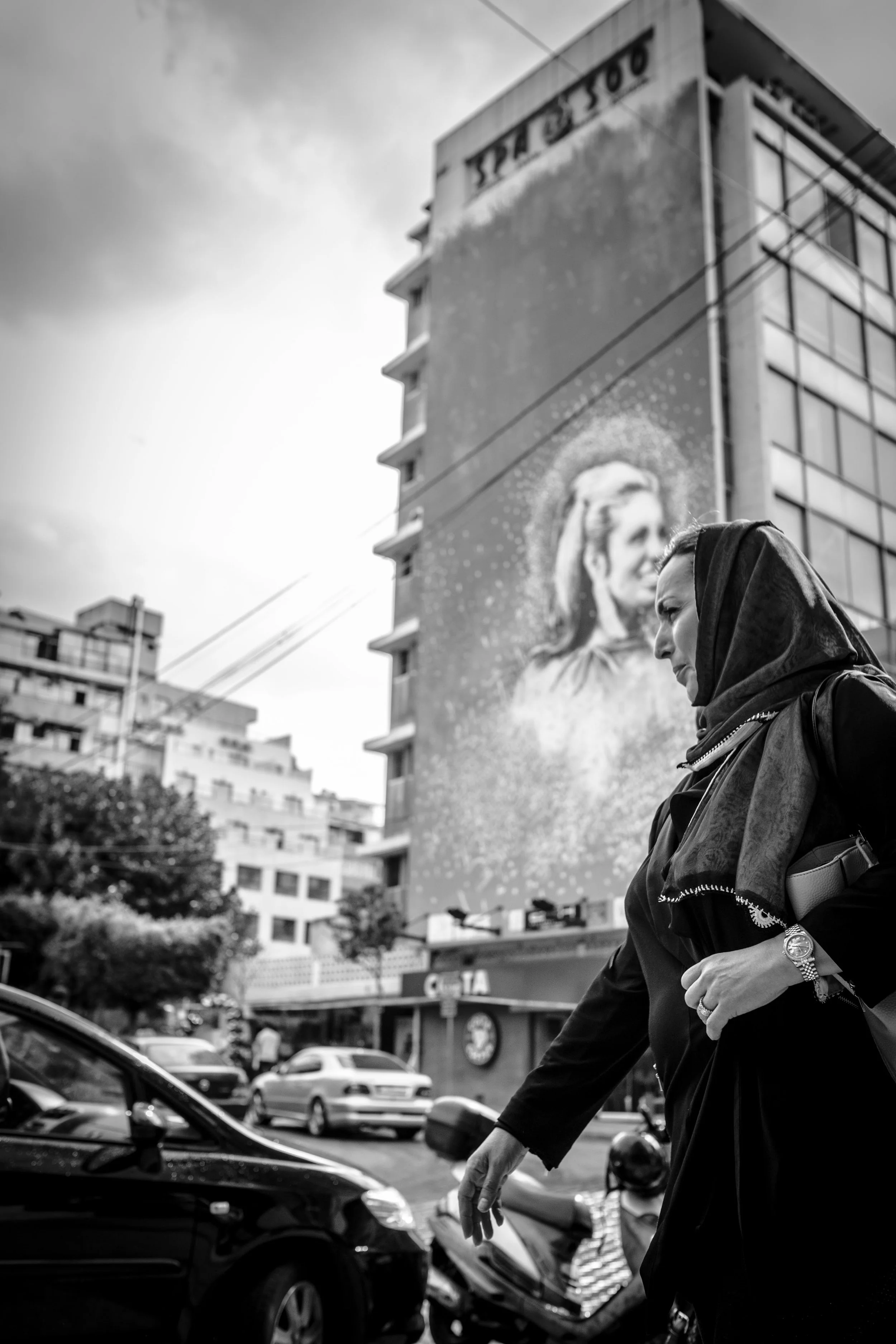 Mujer caminando en la ciudad con edificios de fondo, algunos con publicidad, en un día nublado, en blanco y negro.