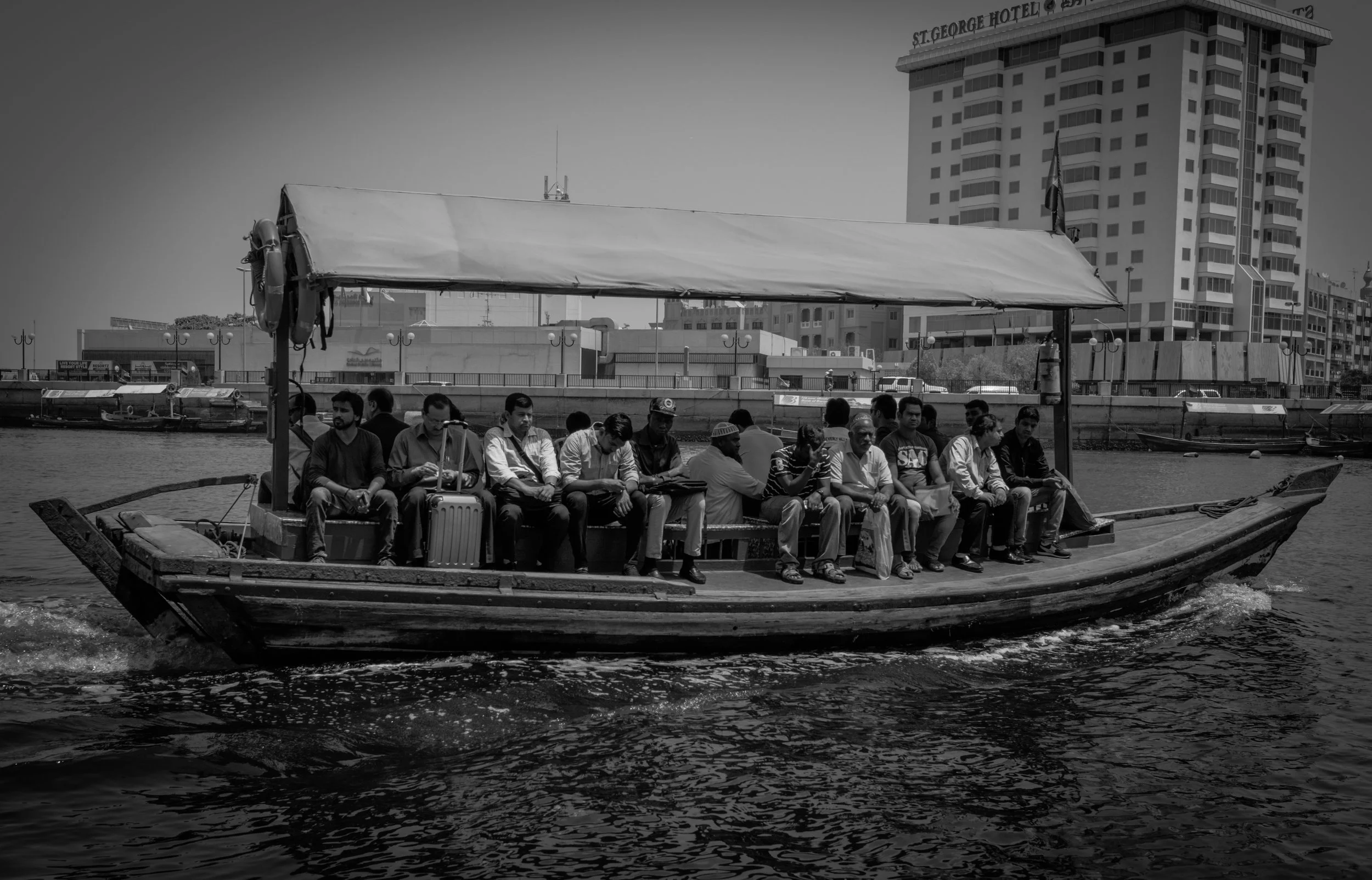 Grupo de personas en un bote navegando por un río en una ciudad con edificios altos al fondo.