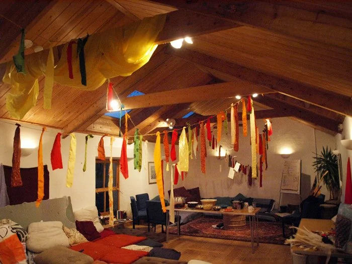 Decorative banners hanging from the ceiling of a cozy living room with wooden beams, sofas, armchairs, and a coffee table.