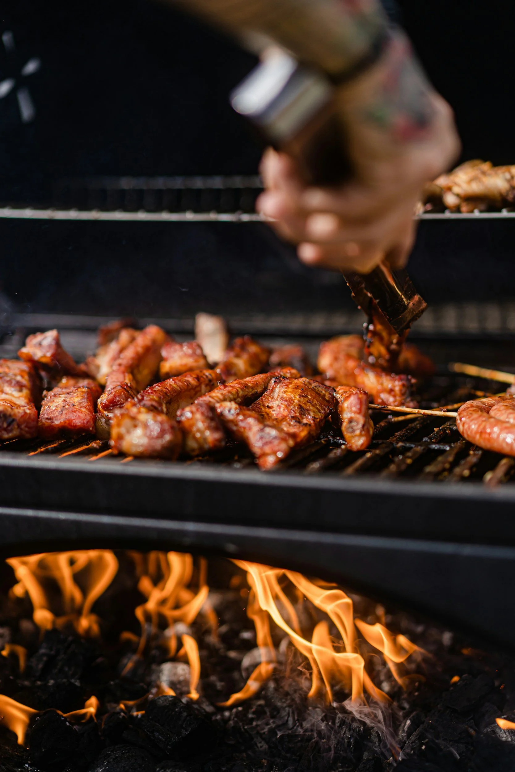 Close-up of meat and shrimp grilling on an outdoor barbecue with flames underneath.