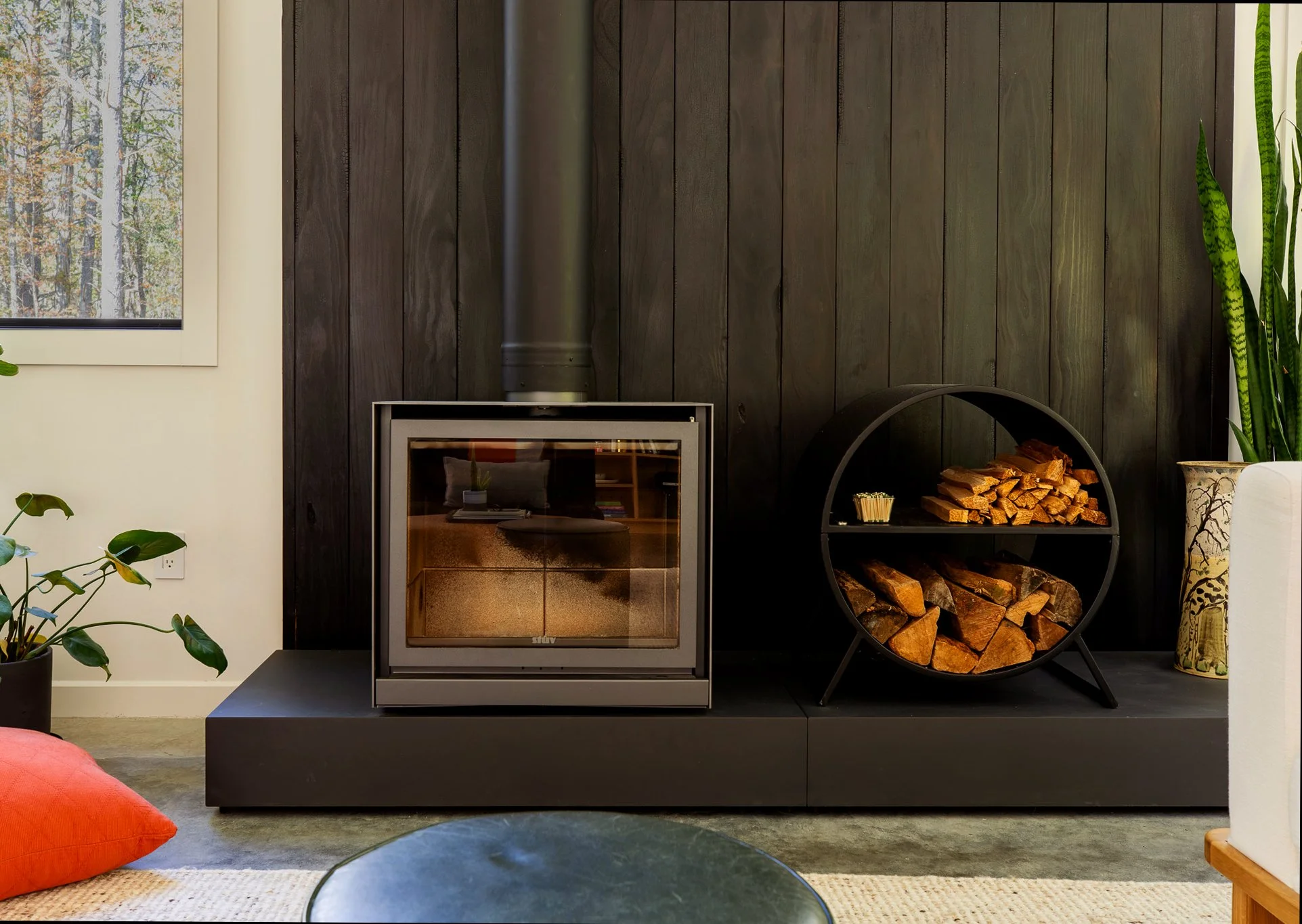 Black wood-burning stove set into a paneled accent wall with round firewood storage.