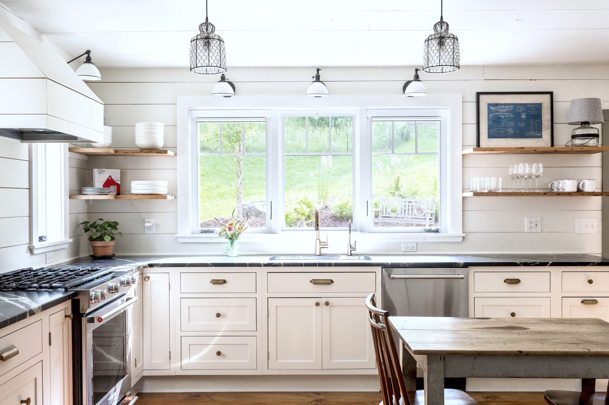 Cottage kitchen with white cabinetry, dark marble countertops, and double window above sink.