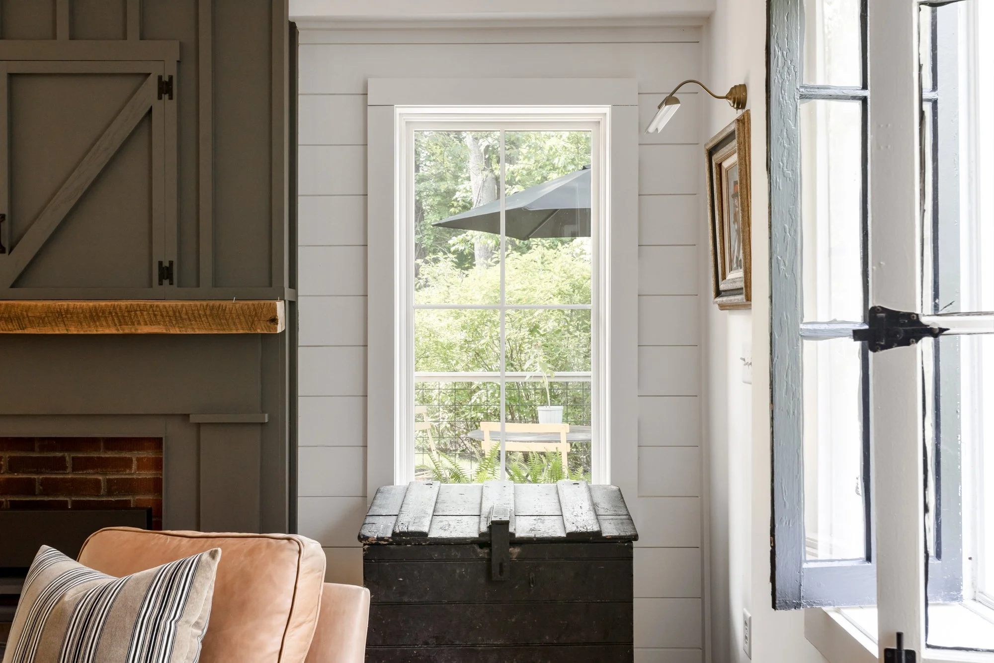 Living room window detail with shiplap walls and vintage black trunk.