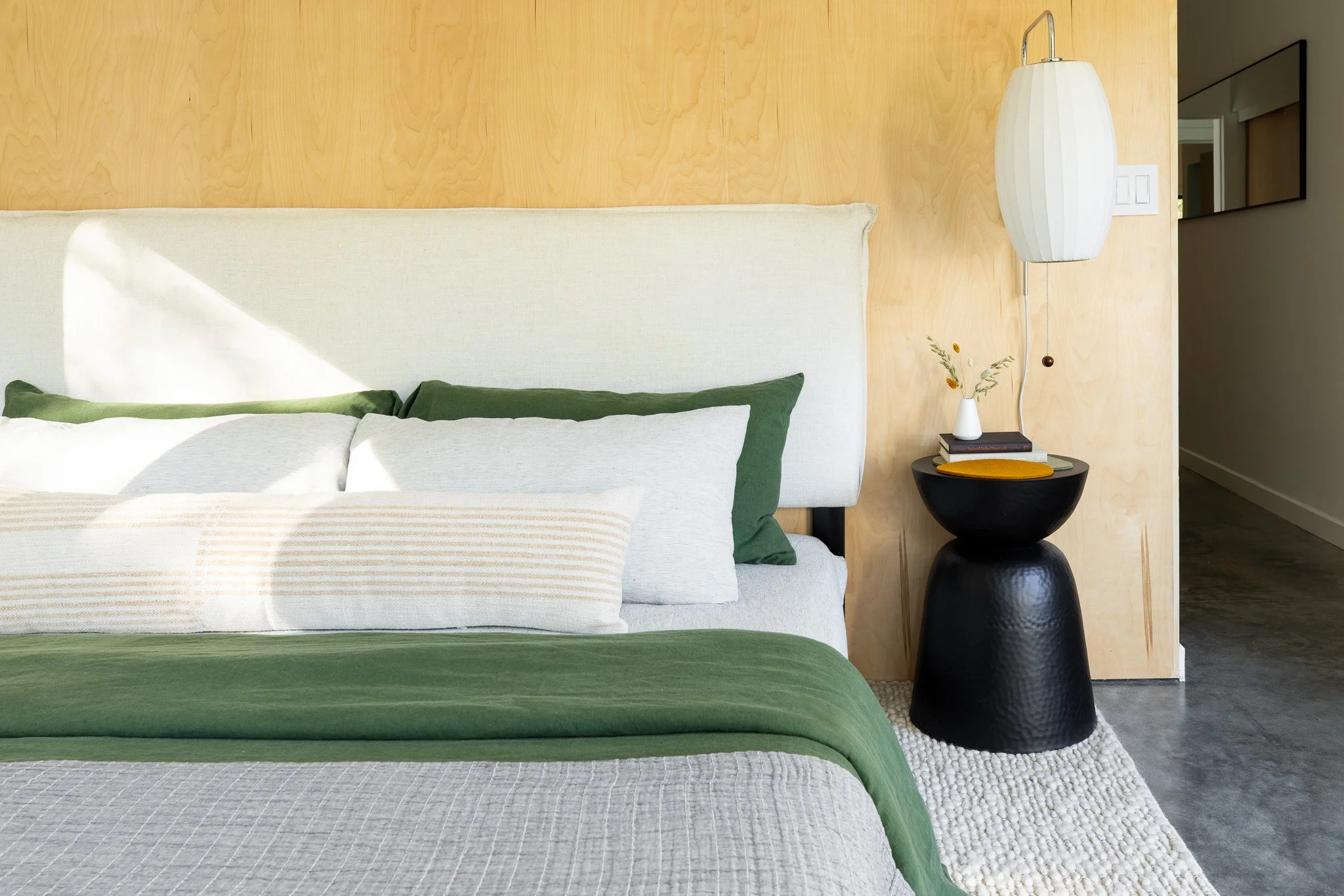 Minimal bedside styling with lamp, plant, and layered textiles.