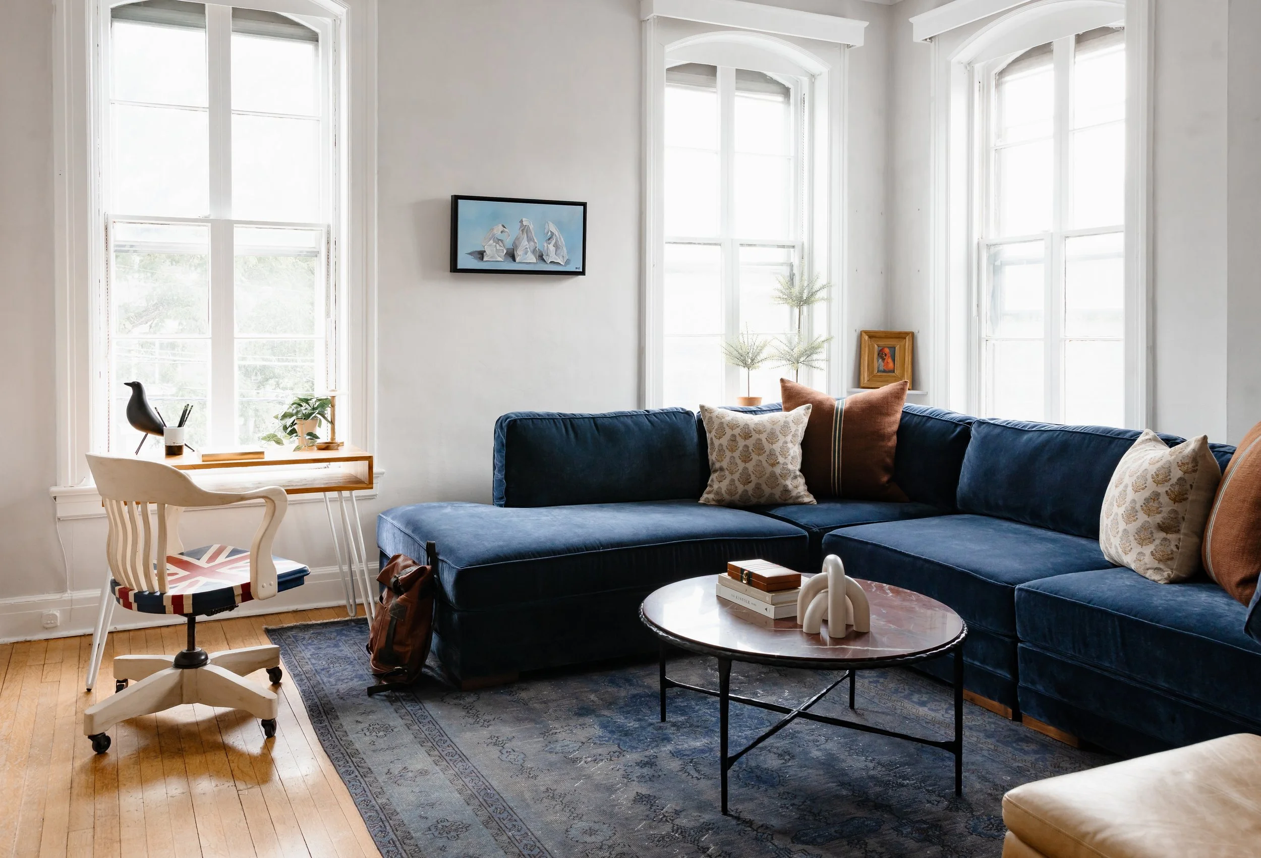 Bright living room with blue sectional sofa, vintage rug, marble coffee table, and tall arched windows.