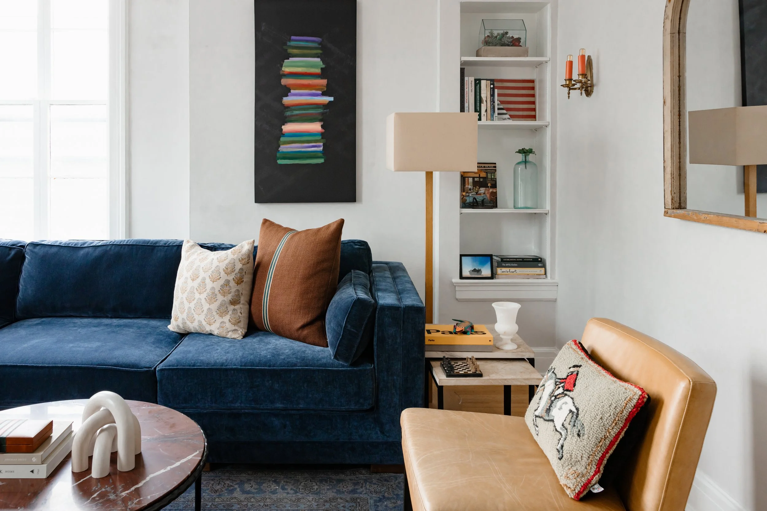 Living room corner with blue sofa, leather chair, built-in shelving, and framed artwork.