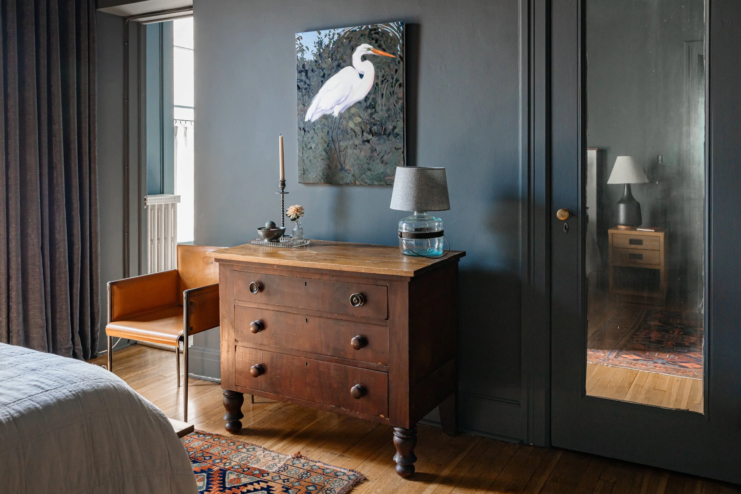 Bedroom with vintage wood dresser, blue walls, and framed artwork above.