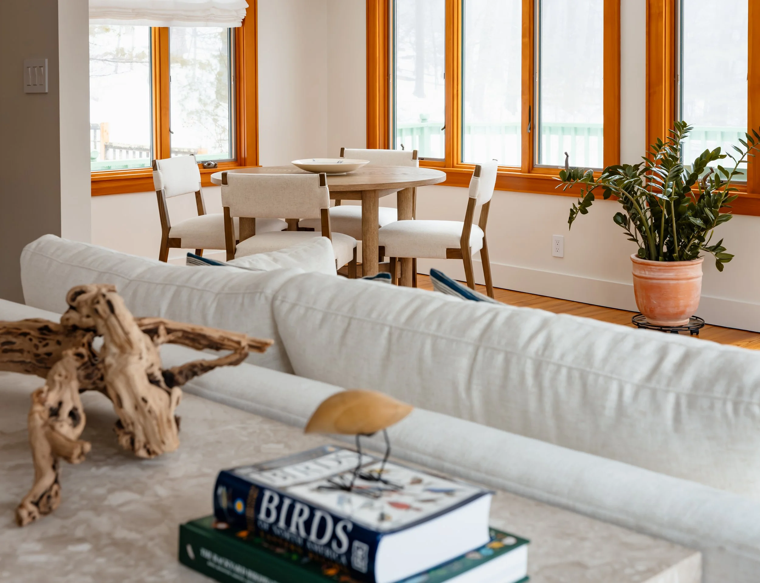 Dining nook with round table, upholstered chairs, and warm wood-trimmed windows.