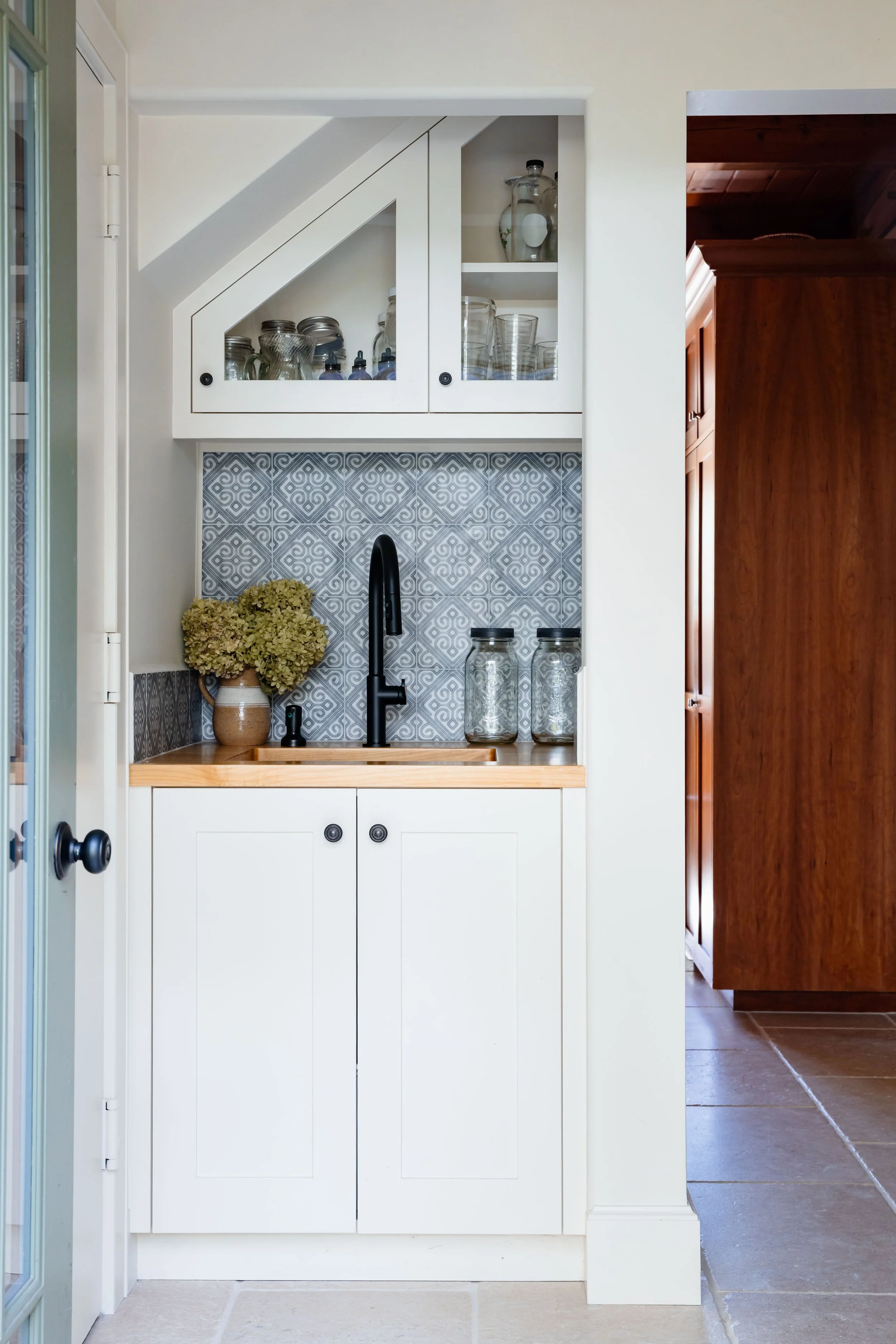 Custom cabinetry with patterned tile backsplash and wood countertop in a renovated straw bale home entry in New Paltz.