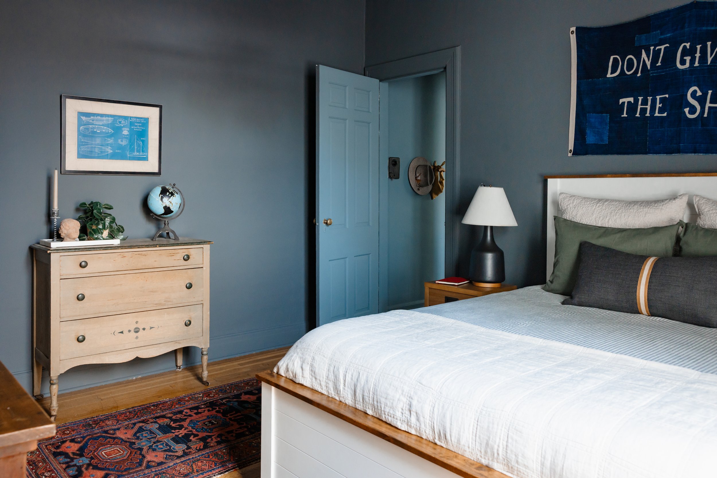 Moody blue bedroom with layered bedding, vintage rug, and antique dresser.