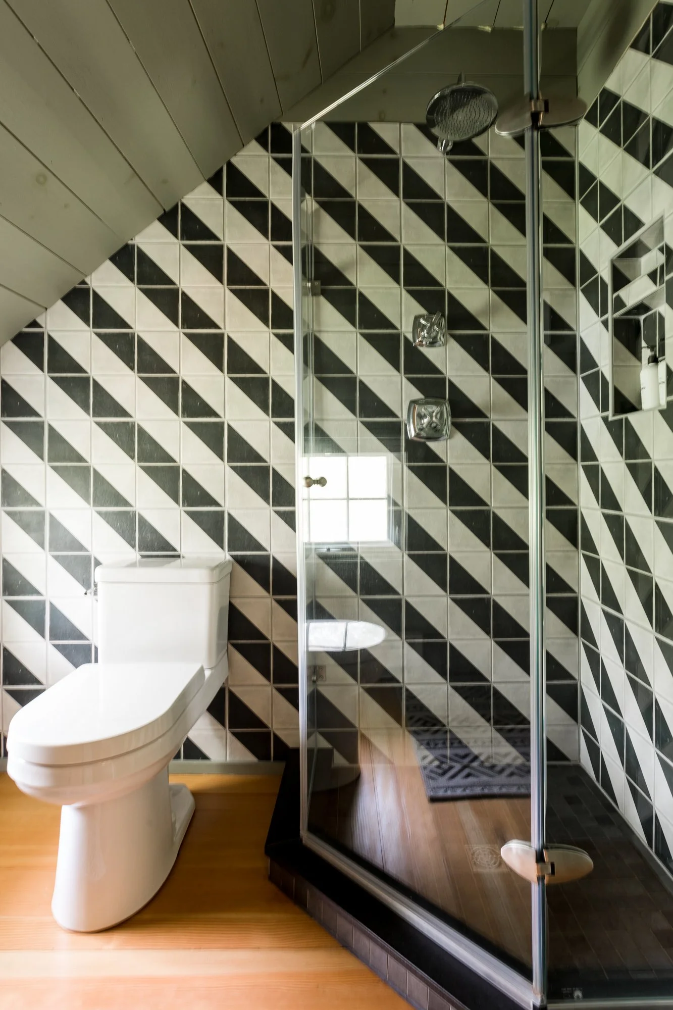 Bathroom with black and white geometric tile shower and glass enclosure.