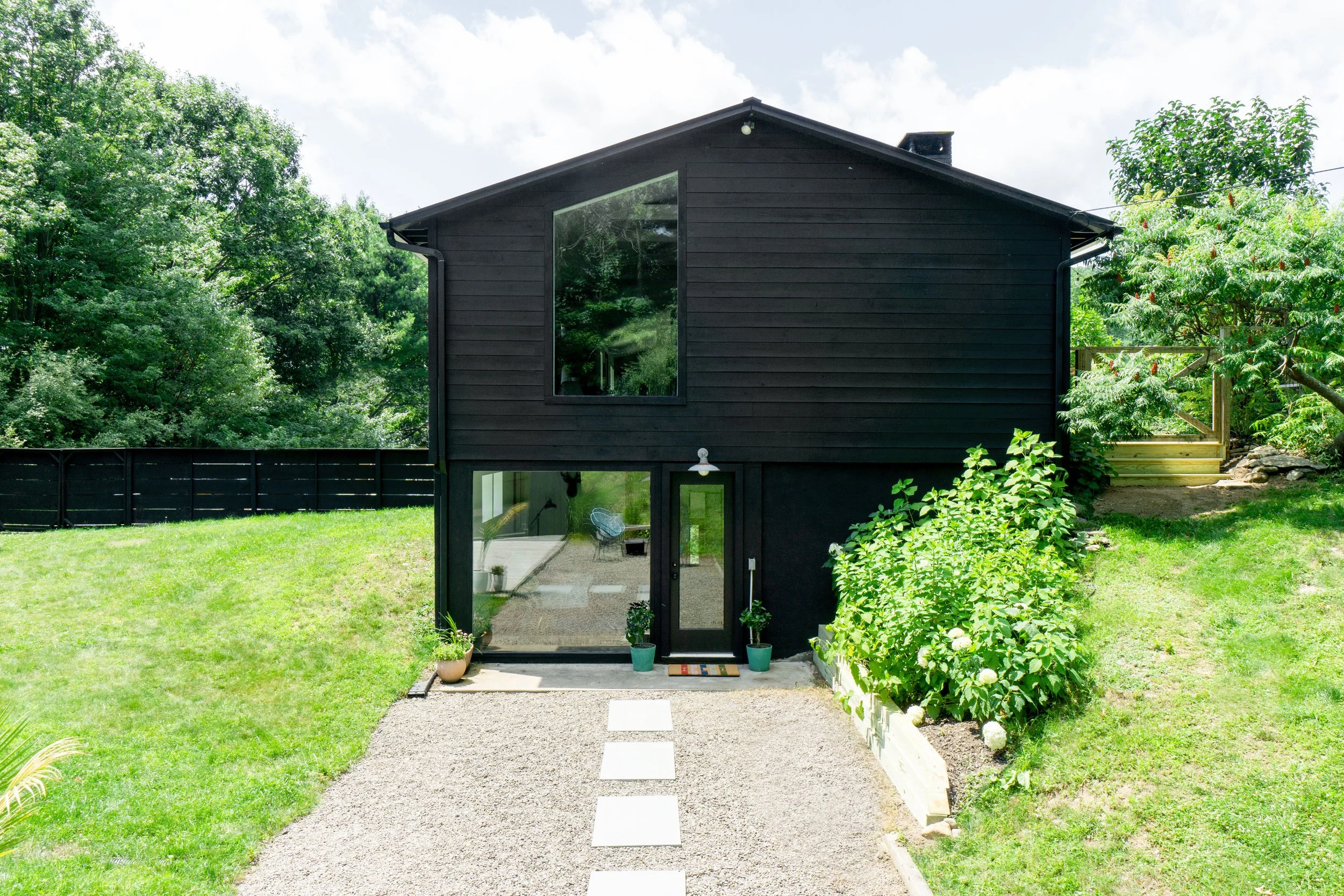 Rear exterior of black modern farmhouse with gravel path and large lower-level windows.