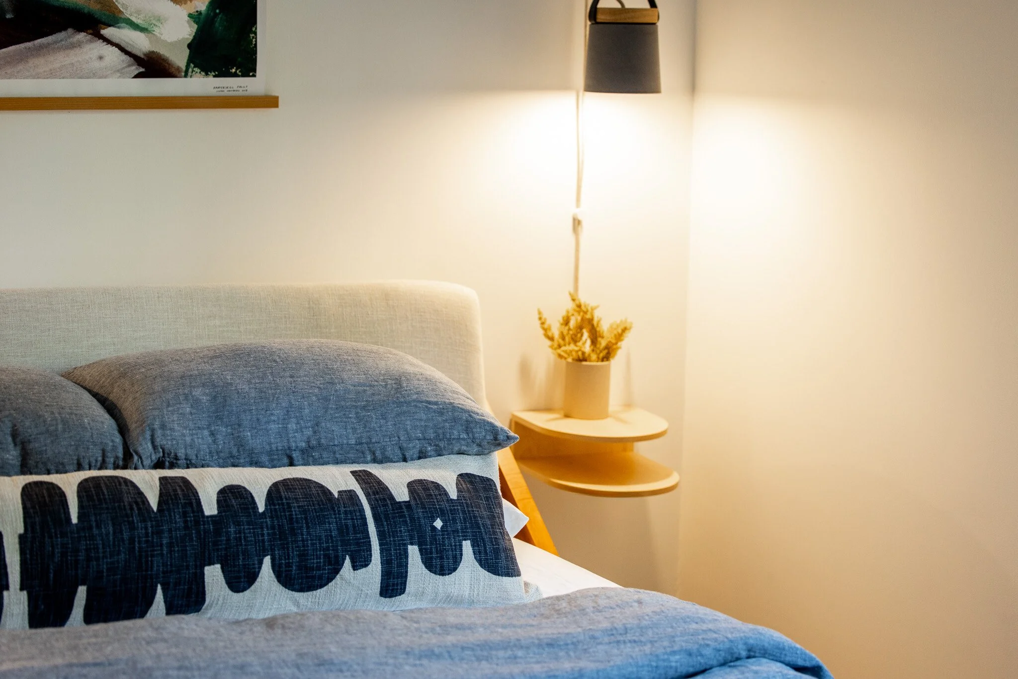 Bedroom detail featuring blue bedding, floating bedside shelf, and wall-mounted sconce.