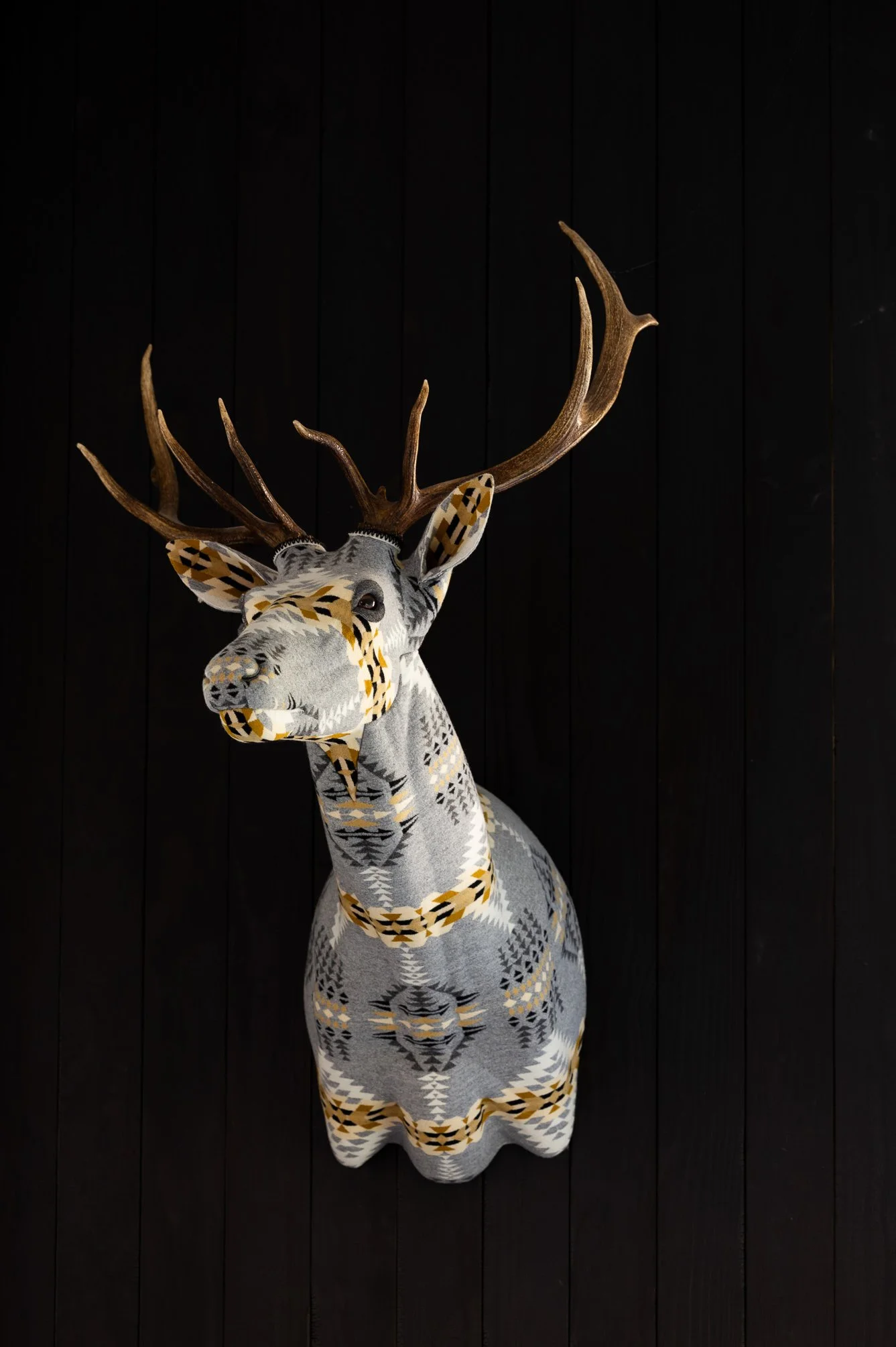 Decorative deer head wall sculpture mounted on a black paneled accent wall.