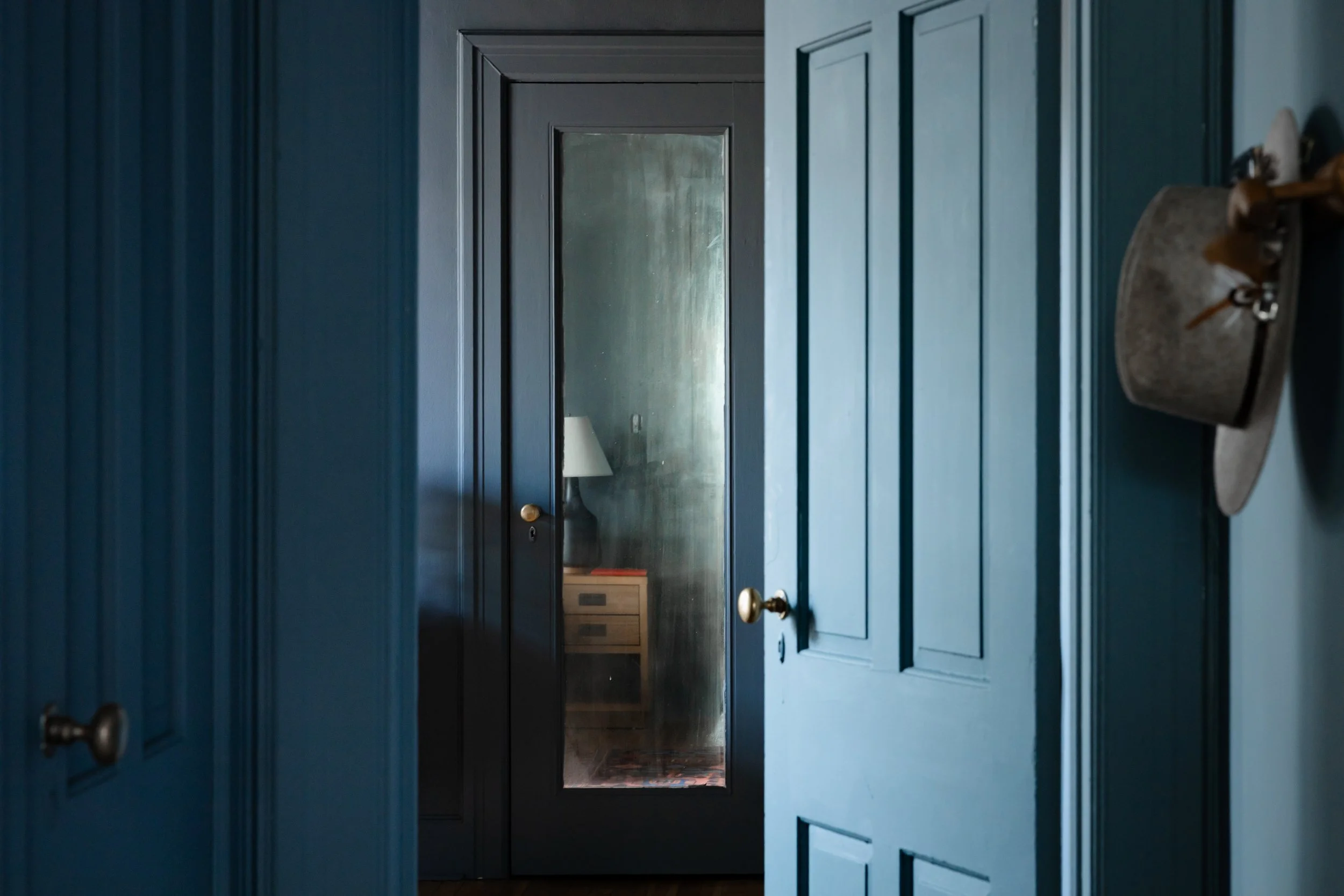 Moody blue hallway with paneled doors and glass inset leading into bedroom.