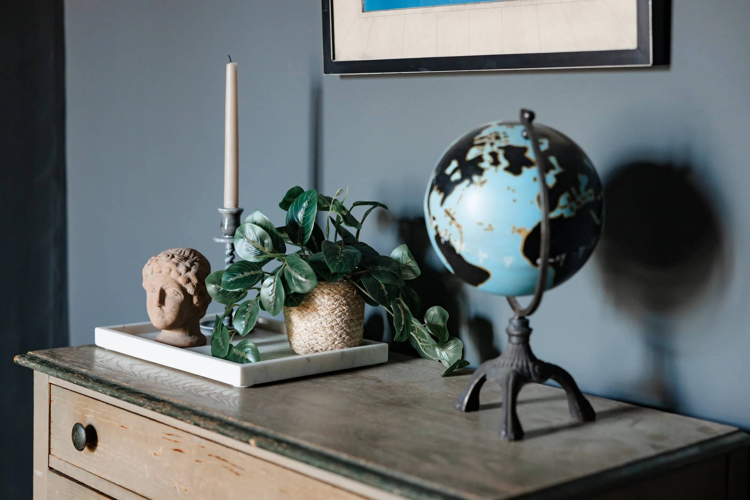 Styled dresser vignette with globe, candleholder, plant, and vintage accessories.