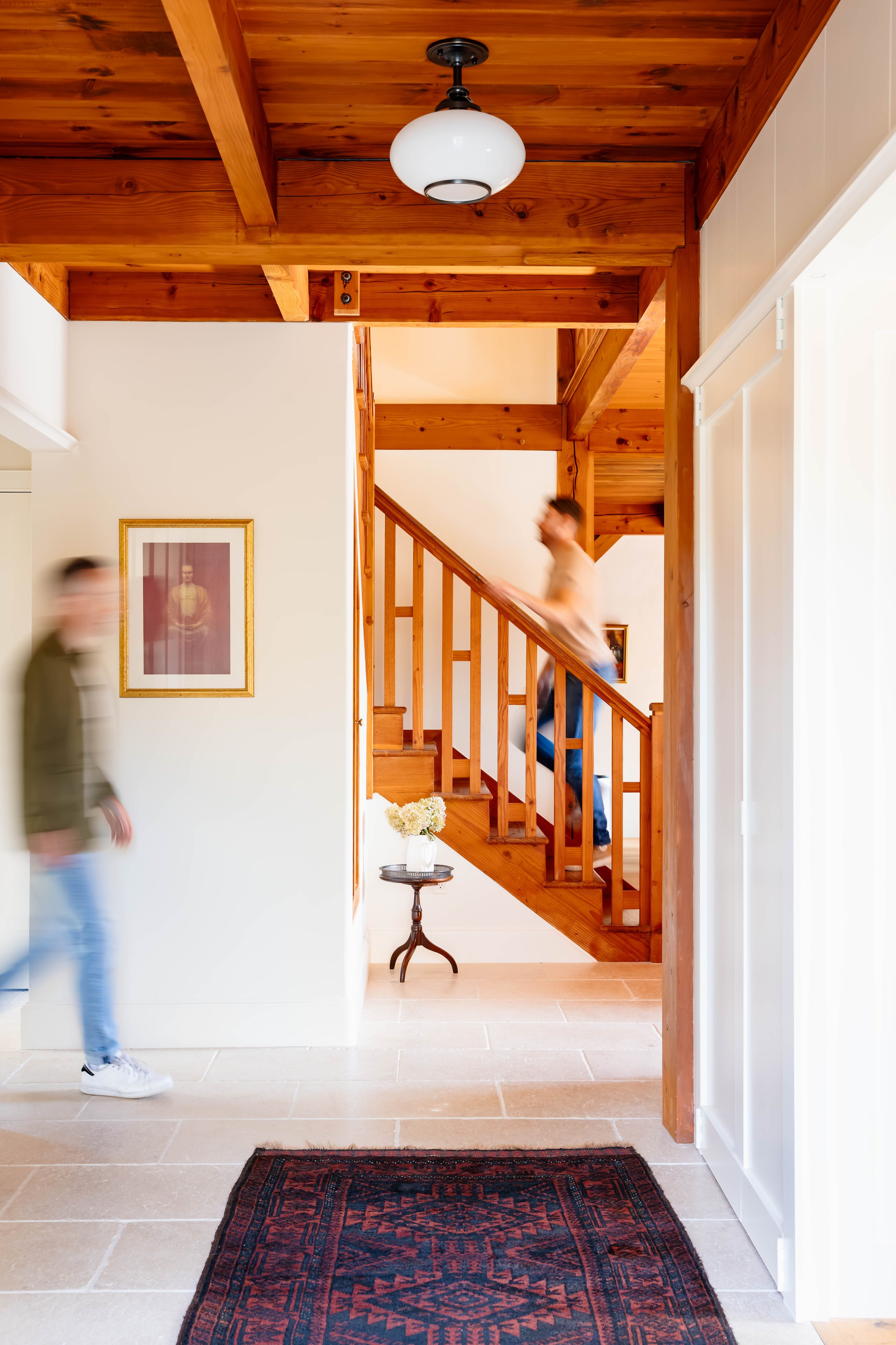 Entry renovation highlighting exposed timber beams, limestone flooring, and staircase in a straw bale home in New Paltz, NY.
