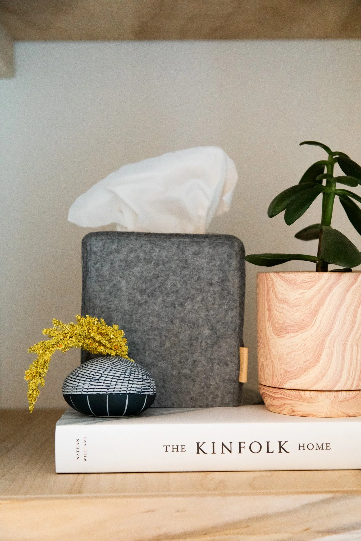 Styled shelf with Kinfolk book, felt tissue box cover, ceramic vase, and small potted plant.