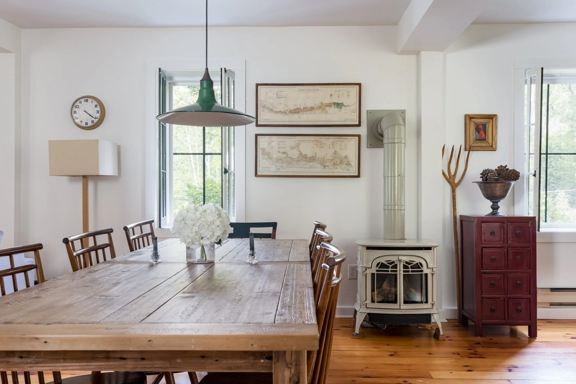 Dining room with rustic wood table, green pendant light, and cast iron wood stove.