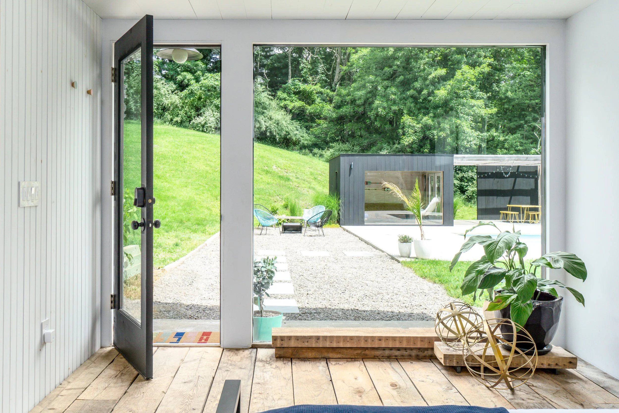Interior view through large picture window and open door overlooking patio and pool house.