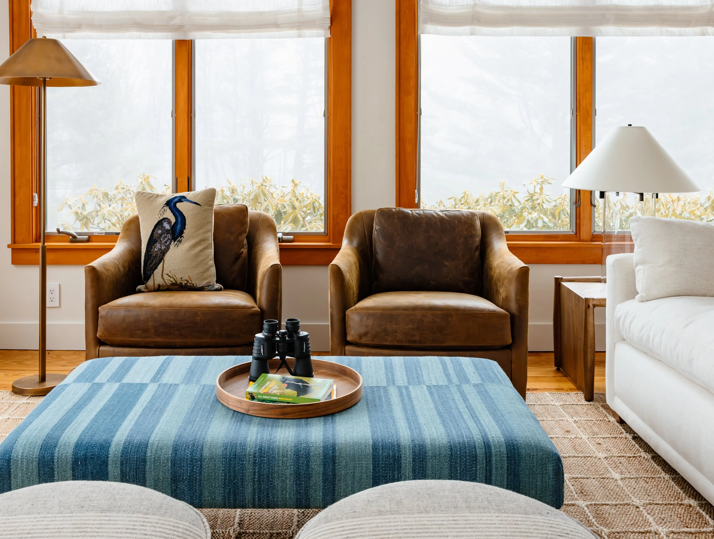 Pair of leather lounge chairs with blue ottoman and styled tray in front of large windows.