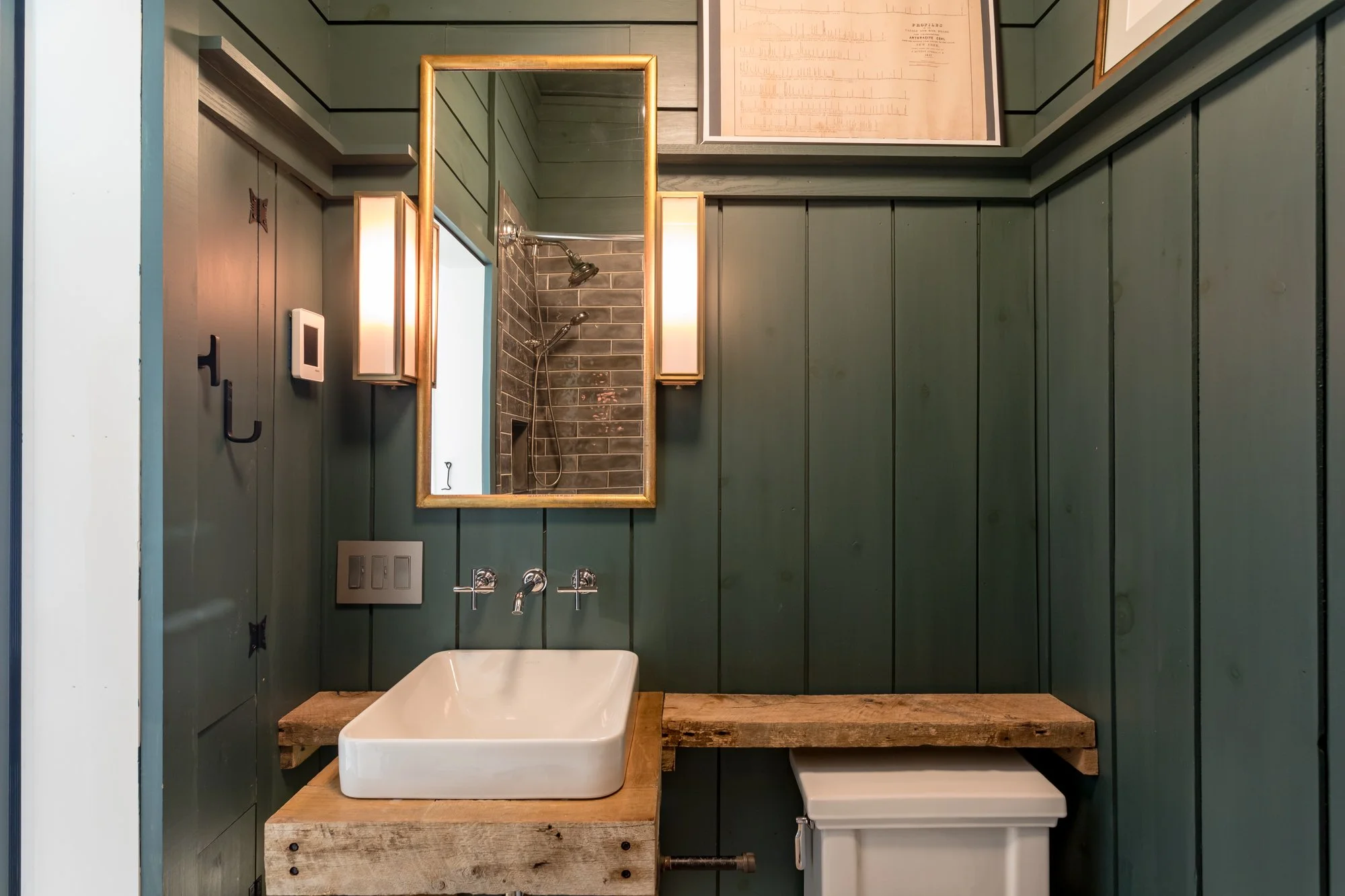 Small bathroom with deep green vertical paneling and wall-mounted sink on rustic wood shelf.
