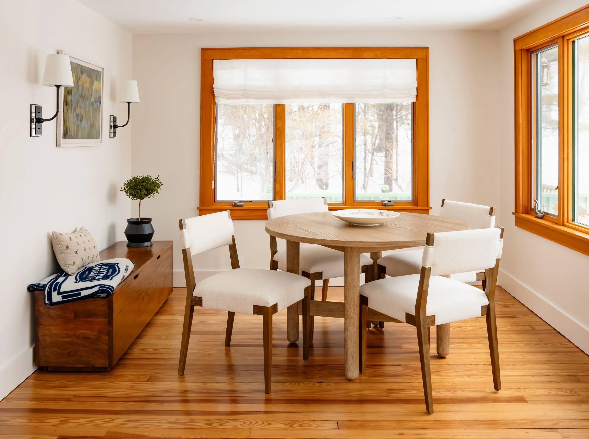 Dining room nook with round wood table, upholstered chairs, and large window bringing in natural light.