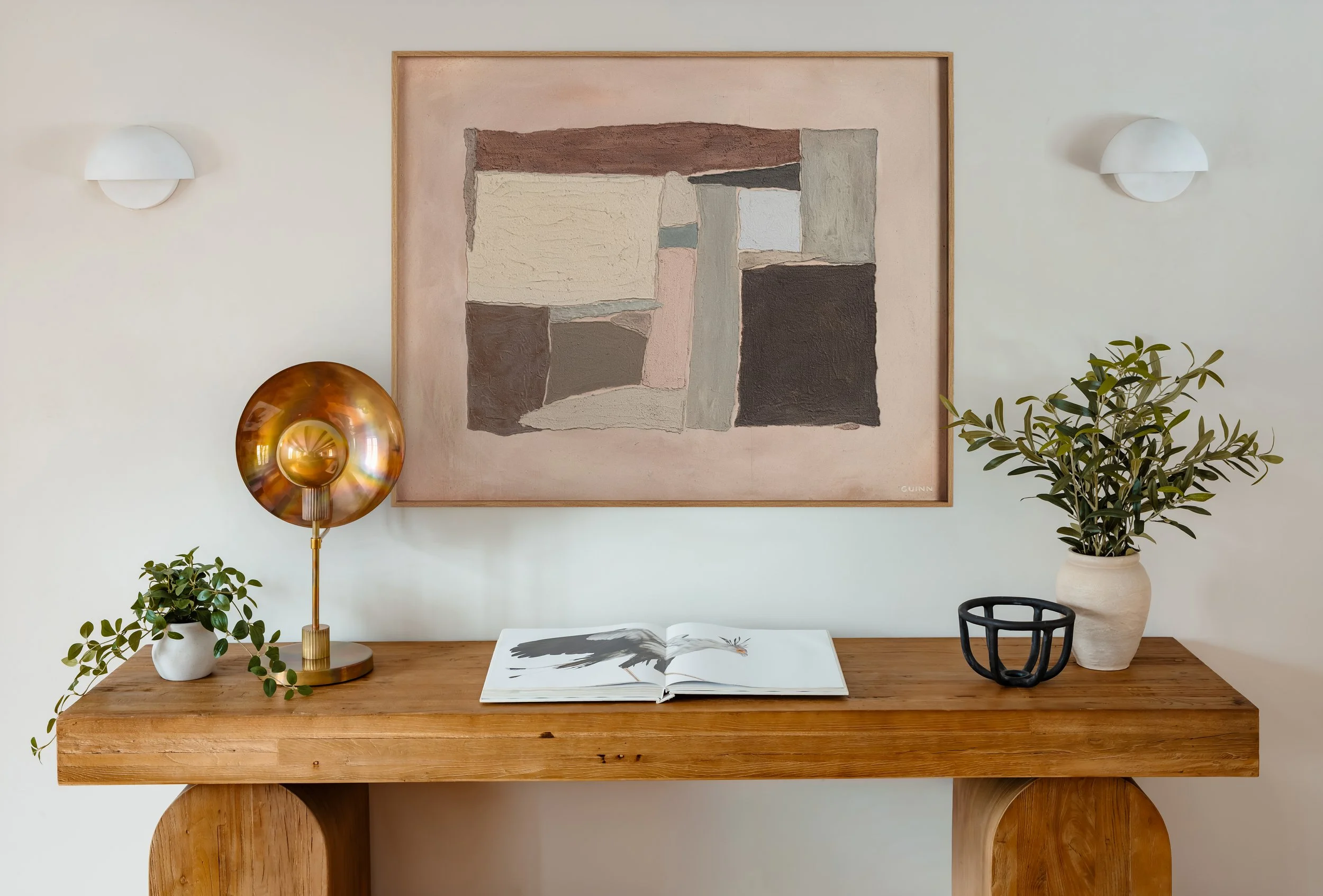 Oak console table styled with abstract art, plants, and warm sculptural lighting.