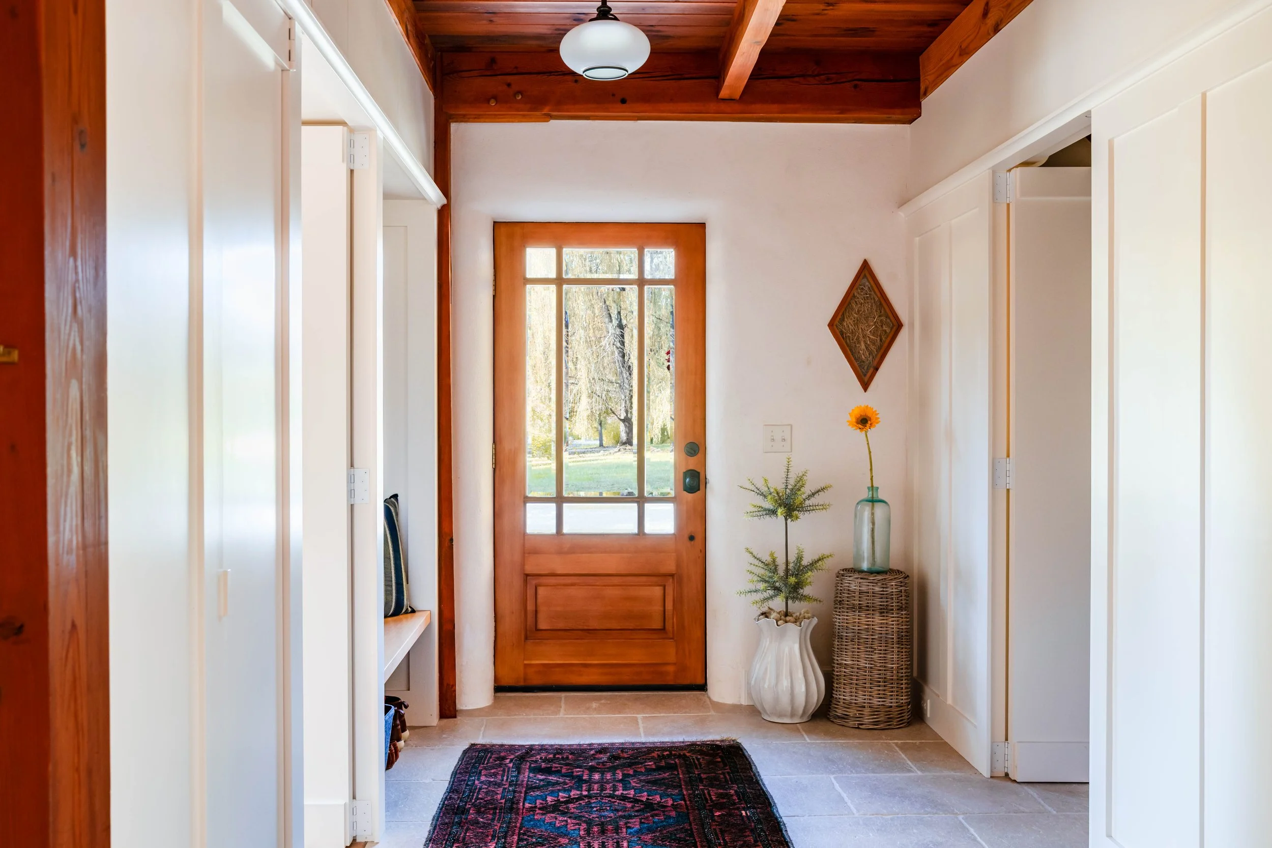 Renovated entry with natural wood front door, limestone tile floors, and soft neutral walls in a New Paltz straw bale home.