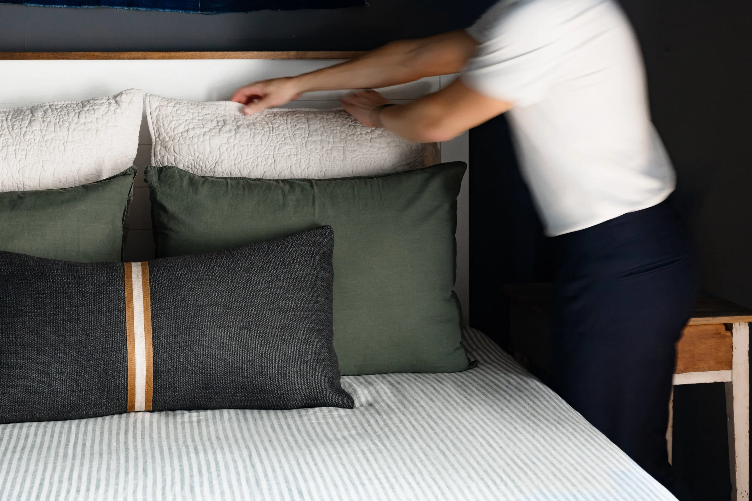 Layered bed styling with green and charcoal pillows against deep blue walls.