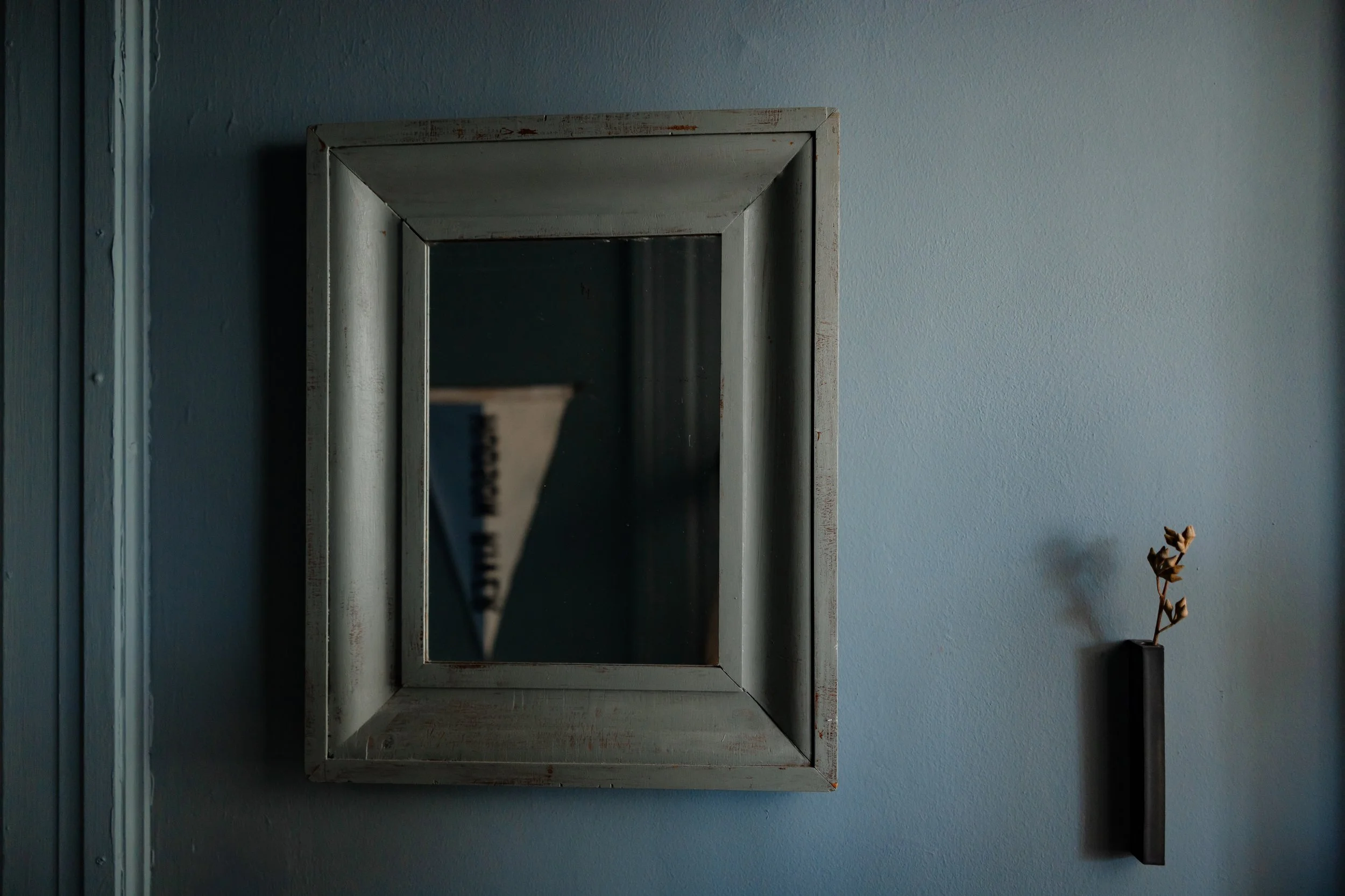 Vintage square mirror on blue wall styled with minimal wall-mounted vessel.