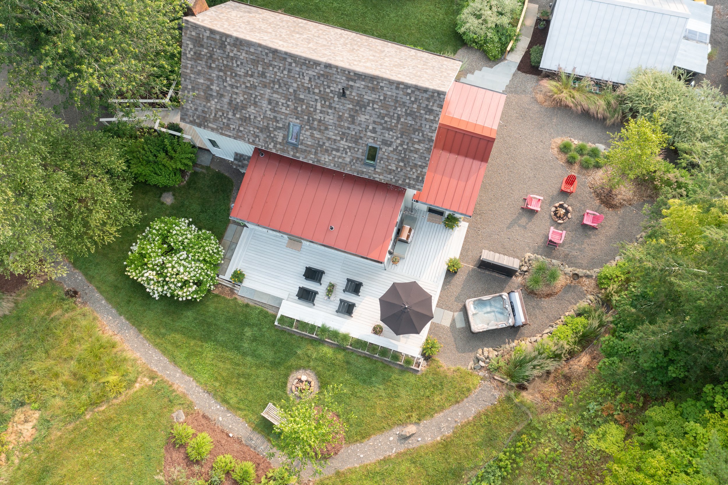 Aerial view of Creeks Lock Cottage with red metal roof, deck, firepit seating area, and landscaped yard.