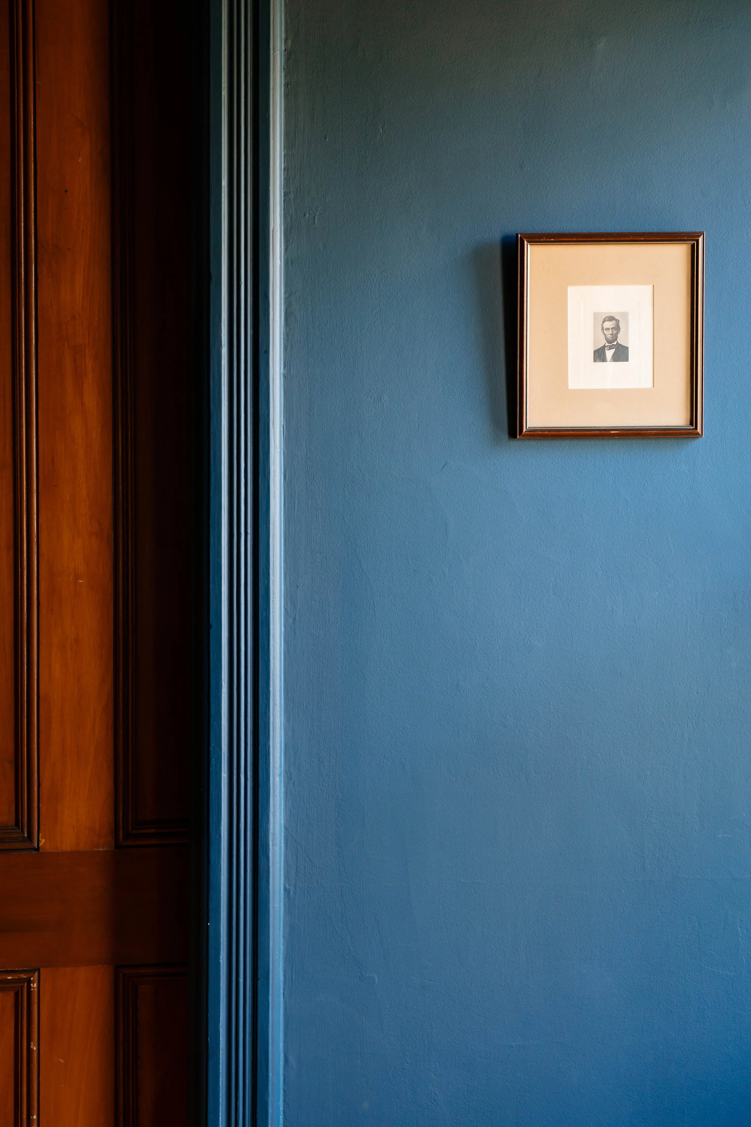 Detail of deep blue painted wall with framed artwork and original wood trim